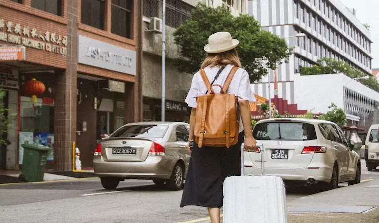 person with a backpack pulling a suitcase down a city road