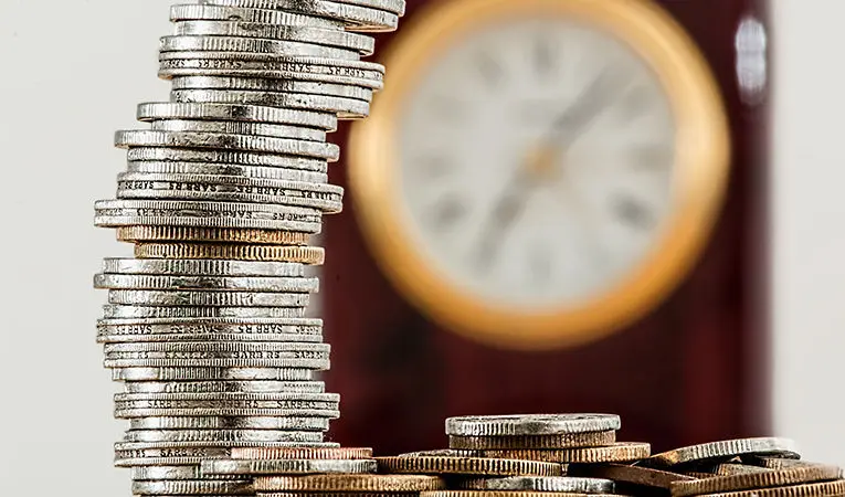 Stacks of coins with clock out of focus in background